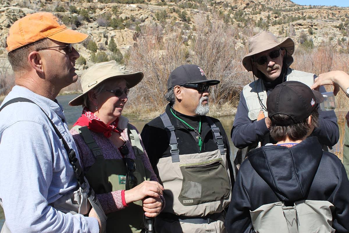 Group of people stand outside, getting instructions on fly fishing.